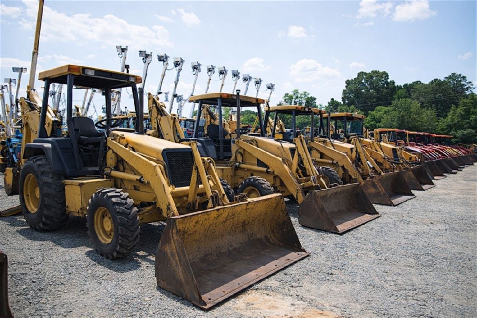 En lång rad med gula traktorgrävare uppställda på en grusplan inför auktion.
