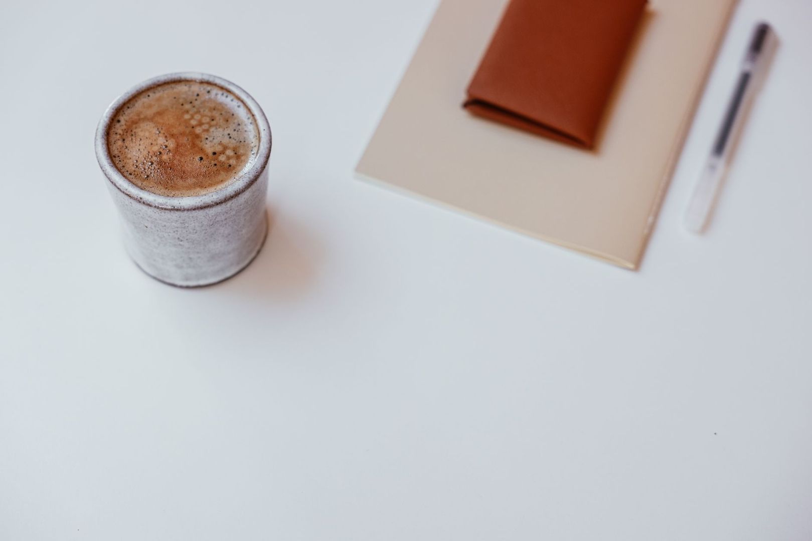Kaffekopp bredvid anteckningsbok och penna på skrivbord